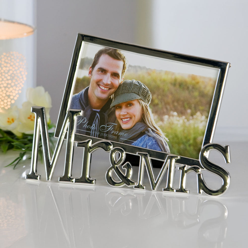 Bilderrahmen "Mr. and Mrs." aus glänzendem, polierten Metall. Am unteren Ende des Fotoaufstellers ist "Mr&MrS" zu lesen, während der eigentliche Rahmen für das Fotoformat 10 x 15 cm schräg darüber angebracht ist.