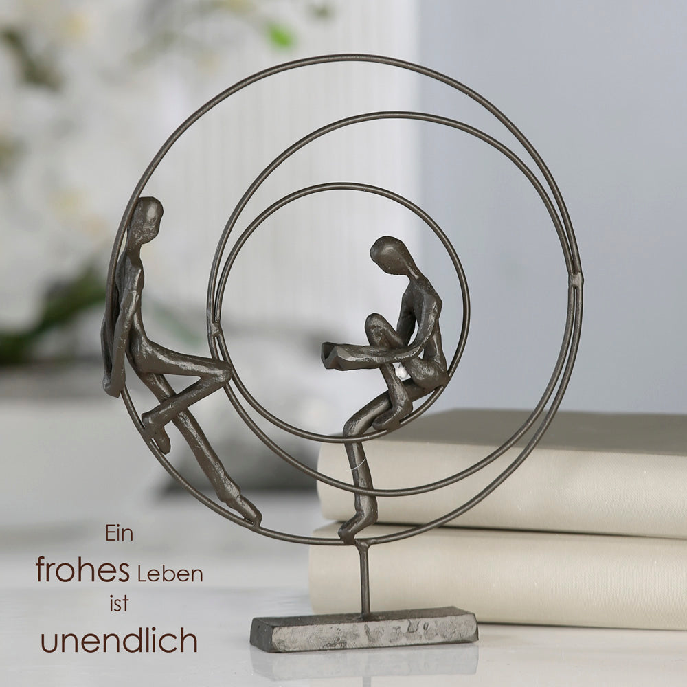 Die Skulptur "Circles" rundes Kunstobjekt aus brüniertem Eisen bestehend aus drei einzelnen Kreisen. Im äußeren und inneren Kreis sitzt je eine Figur. Die Figur im inneren Kreis liest ein Buch.