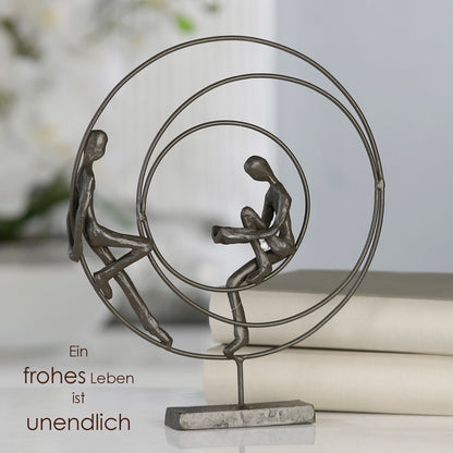 Die Skulptur "Circles" rundes Kunstobjekt aus brüniertem Eisen bestehend aus drei einzelnen Kreisen. Im äußeren und inneren Kreis sitzt je eine Figur. Die Figur im inneren Kreis liest ein Buch.