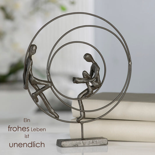 Die Skulptur "Circles" rundes Kunstobjekt aus brüniertem Eisen bestehend aus drei einzelnen Kreisen. Im äußeren und inneren Kreis sitzt je eine Figur. Die Figur im inneren Kreis liest ein Buch.