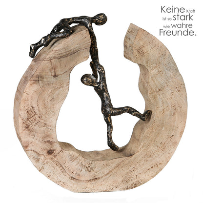 Die Skulptur "Teamwork" besteht aus einer massiven, naturbelassenen Baumscheibe aus Mango Holz. Auf und im Inneren der Skulptur befinden sich zwei miteinander verbundene Figuren, die Teamarbeit symbolisieren sollen. Der Figur im Inneren wird aus einer ausweglosen zu scheinenden Situation geholfen.