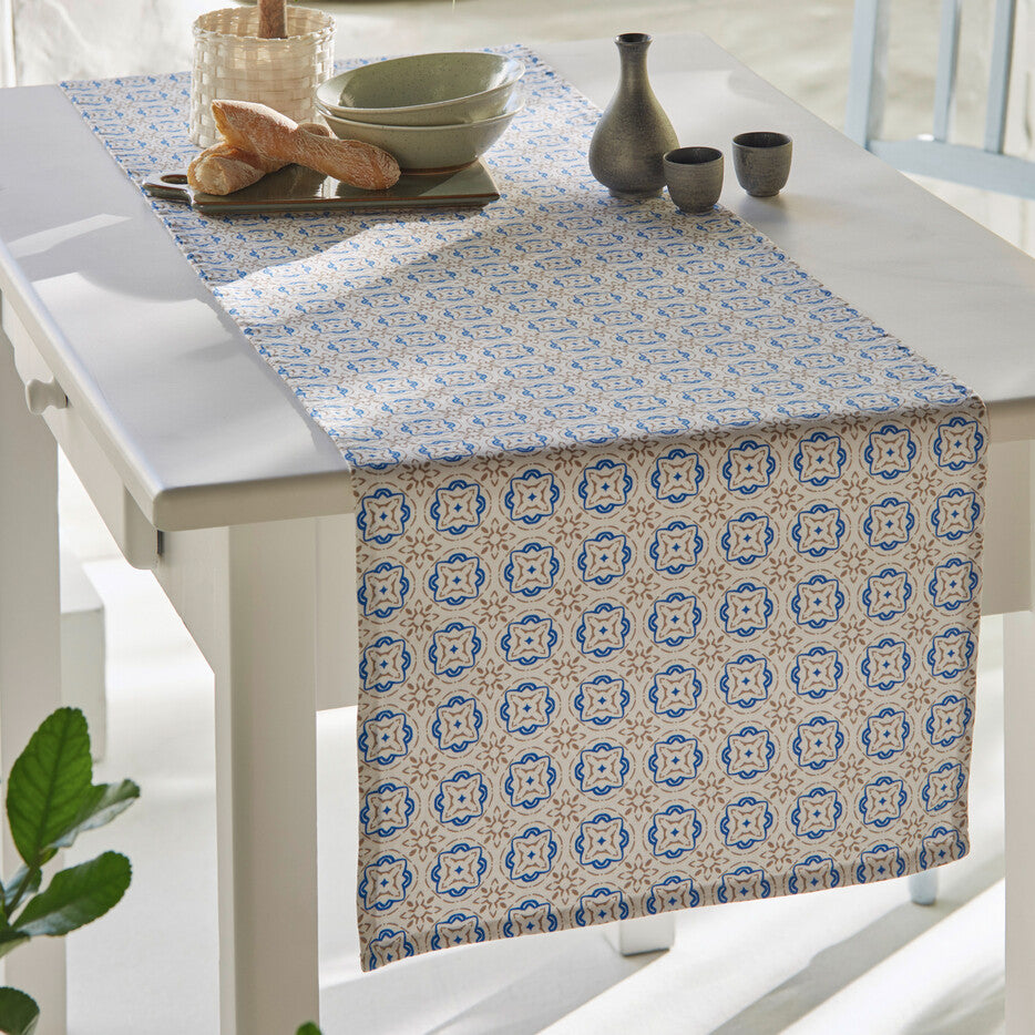 Tischläufer "Santorin" aus einem weißen Grundstoff mit einem geometrischen Mosaik-Design in den zurückhaltenden Farben beige und blau.