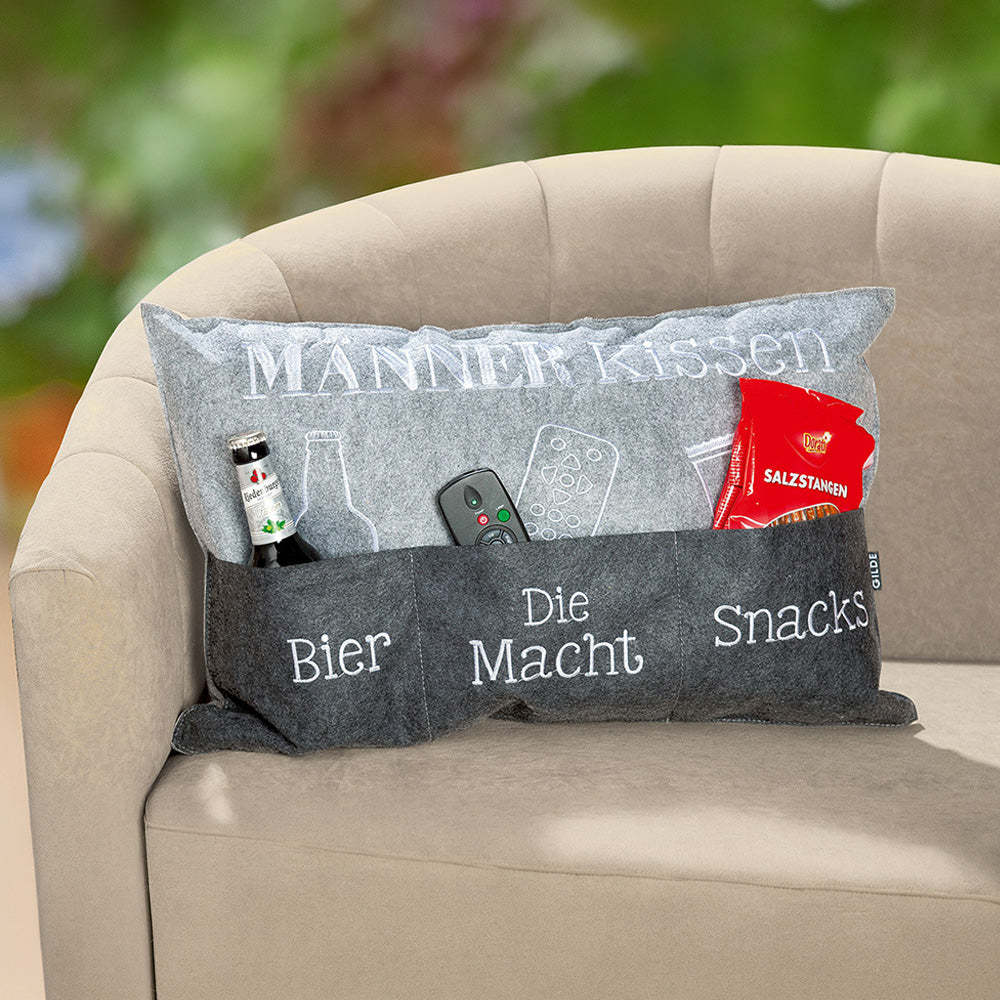 Graues Kissen aus Filz mit drei Aufbewahrungstaschen für Bier, Fernbedienung und Snacks. Die drei Taschen auf der Vorderseite des Kissens sind beschriftet mit "Bier", "Die Macht" und "Snacks"