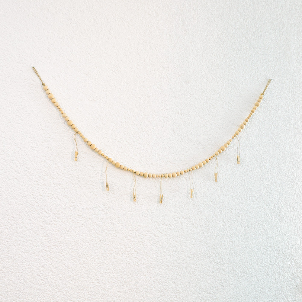 DECCARO Fotoaufhänger Cord, Fotoaufhänger aus einer hellen horizontalen Baumwollschnur auf die hellen Holzperlen aufgereiht sind. An dieser Schnur sind sechs vertikal ausgerichtete Baumwollschnüre mit Holzperlen und kleinen Holzklammern befestigt, an den Fotos und Postkarten aufgehangen werden können. 