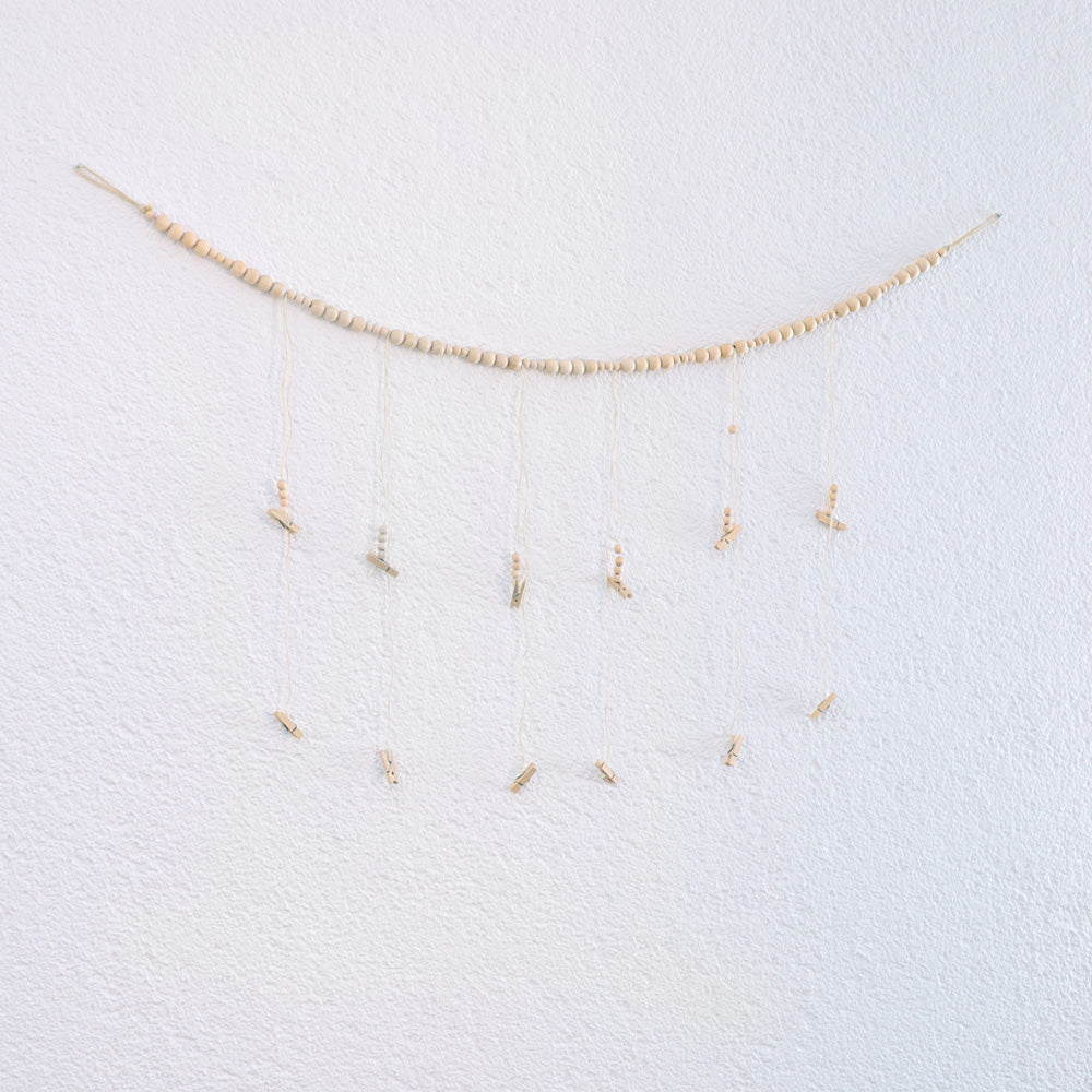 DECCARO Fotoaufhänger Cord, Fotoaufhänger aus einer hellen horizontalen Baumwollschnur auf die hellen Holzperlen aufgereiht sind. An dieser Schnur sind sechs vertikal ausgerichtete Baumwollschnüre mit Holzperlen und kleinen Holzklammern befestigt, an den Fotos und Postkarten aufgehangen werden können. 