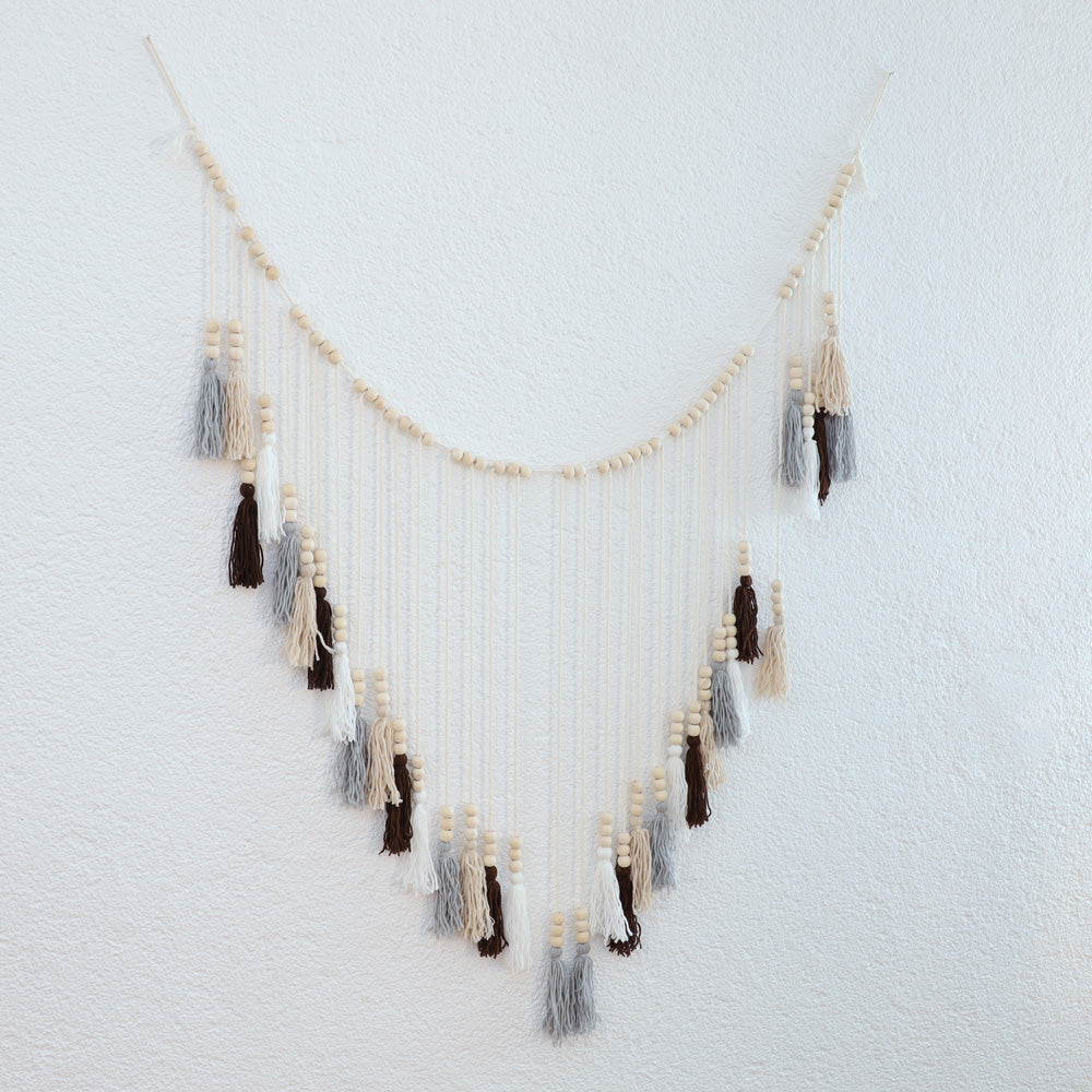 DECCARO Makramee Girlande Tassel. Kombination aus naturfarbenem Baumwollseil mit kleinen Holzperlen und vom Baumwollseil nach unten hängenden Baumwollquasten in den Farben weiß, beige, grau und braun. Oberhalb der Quasten befinden sich an jeder Quaste je drei Holzperlen.