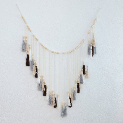 DECCARO Makramee Girlande Tassel. Kombination aus naturfarbenem Baumwollseil mit kleinen Holzperlen und vom Baumwollseil nach unten hängenden Baumwollquasten in den Farben weiß, beige, grau und braun. Oberhalb der Quasten befinden sich an jeder Quaste je drei Holzperlen.