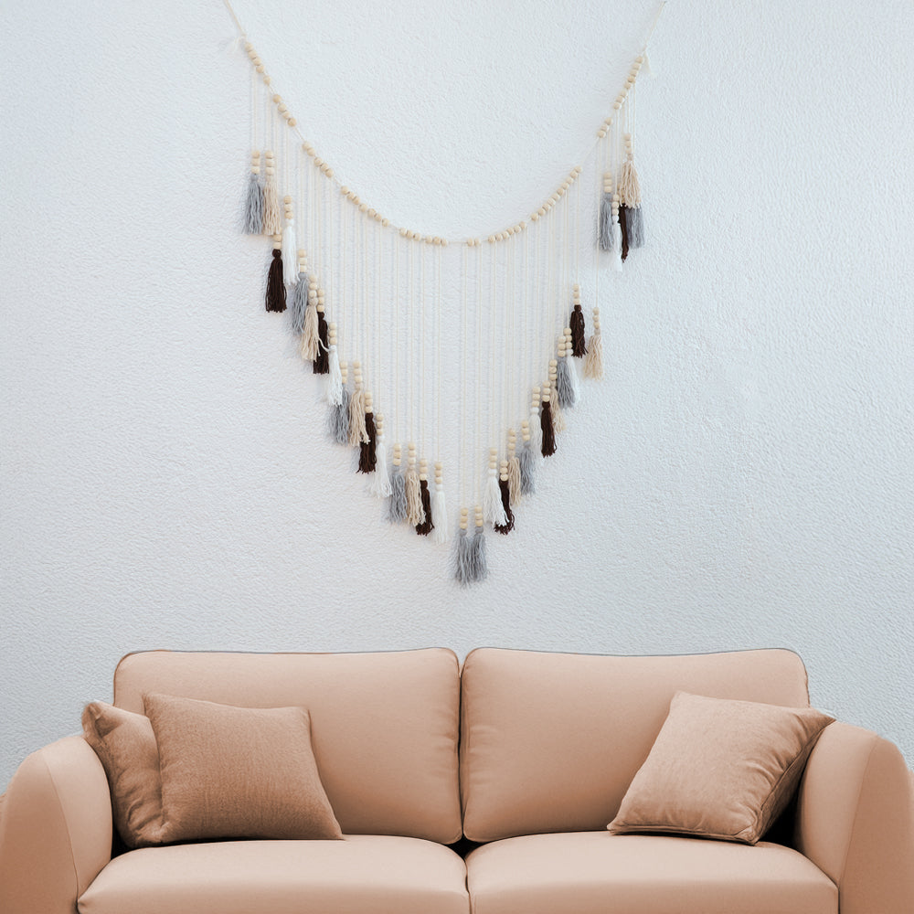 DECCARO Makramee Girlande Tassel. Kombination aus naturfarbenem Baumwollseil mit kleinen Holzperlen und vom Baumwollseil nach unten hängenden Baumwollquasten in den Farben weiß, beige, grau und braun. Oberhalb der Quasten befinden sich an jeder Quaste je drei Holzperlen.