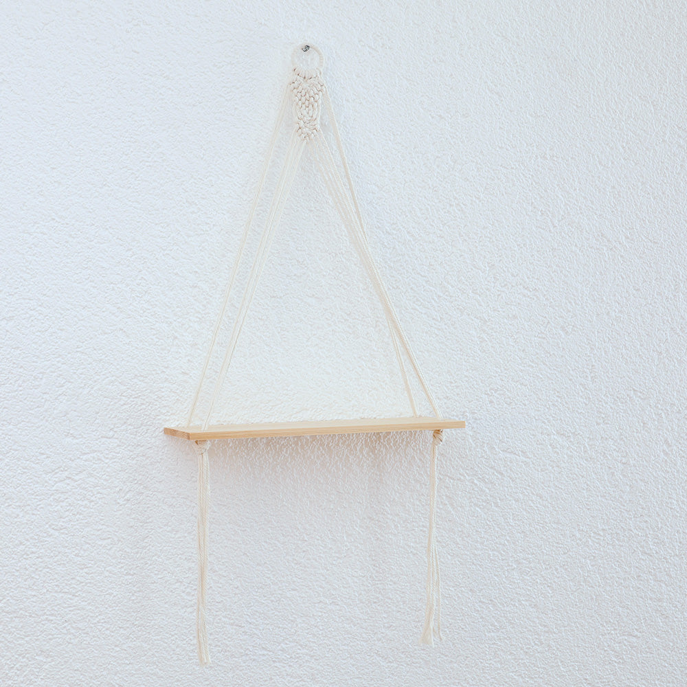 DECCARO Makramee-Hängeregal Swing. Runder Holzaufhänger ummantelt mit einem Baumwollseil. Darunter befindet sich ein Makramee Knotenmuster, von dem aus Baumwollseile mit einem stabilen Holzbrett verknüpft sind.