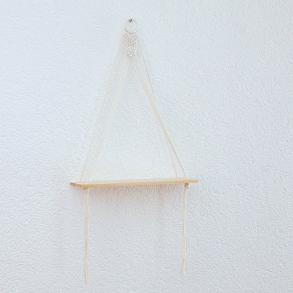 DECCARO Makramee-Hängeregal Swing. Runder Holzaufhänger ummantelt mit einem Baumwollseil. Darunter befindet sich ein Makramee Knotenmuster, von dem aus Baumwollseile mit einem stabilen Holzbrett verknüpft sind.