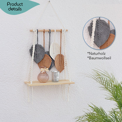 DECCARO Makramee-Hängeregal. Vertikale Holzstange an der Baumwollseile befestigt sind, die mit einem stabilen, schmalen Holzbrett am unteren Ende verknüpft sind. Weiterhin sind an der Holzstange mehrere Baumwollschnüre befestigt, dessen Ende rotbraune, weiße und graue Baumwollschnüre in Blätterform bilden. 