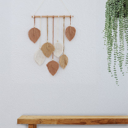 DECCARO Makramee Wanddekoration „Bar“ ockerfarben im Boho-Stil. Naturbelassene horizontale Holzstange an der Baumwollseile mit Holzperlen befestigt sind. Das Ende der Baumwollseile bilden creme, beige und ockerfarbene Baumwollschnüre in Blätteroptik. 