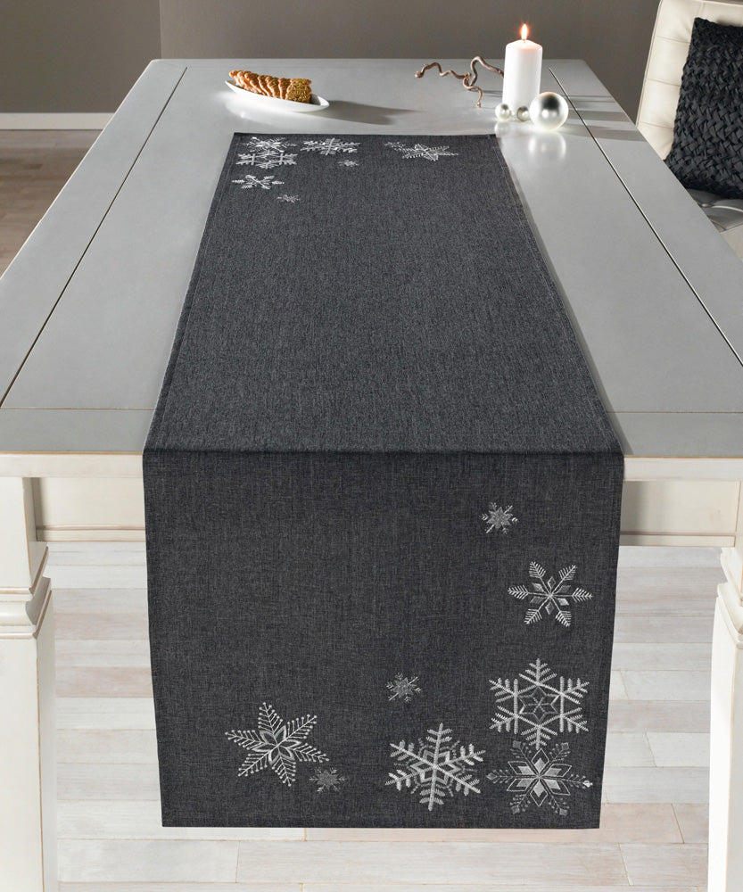 Tischläufer Silberkristall aus einem puristischen Grundstoff, in zeitlosen Grautönen meliert, detailliert bestickt mit filigranen Eiskristallen in schimmerndem Weiß und funkelndem Silber.