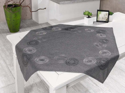 Tischdecke "Kringel"aus einem puristischen Grundstoff in zeitlosen Grautönen meliert mit aufwändigen Kreismotiven aus seidig glänzendem Garn in Weiß, Grau und Schwarz bestickt.