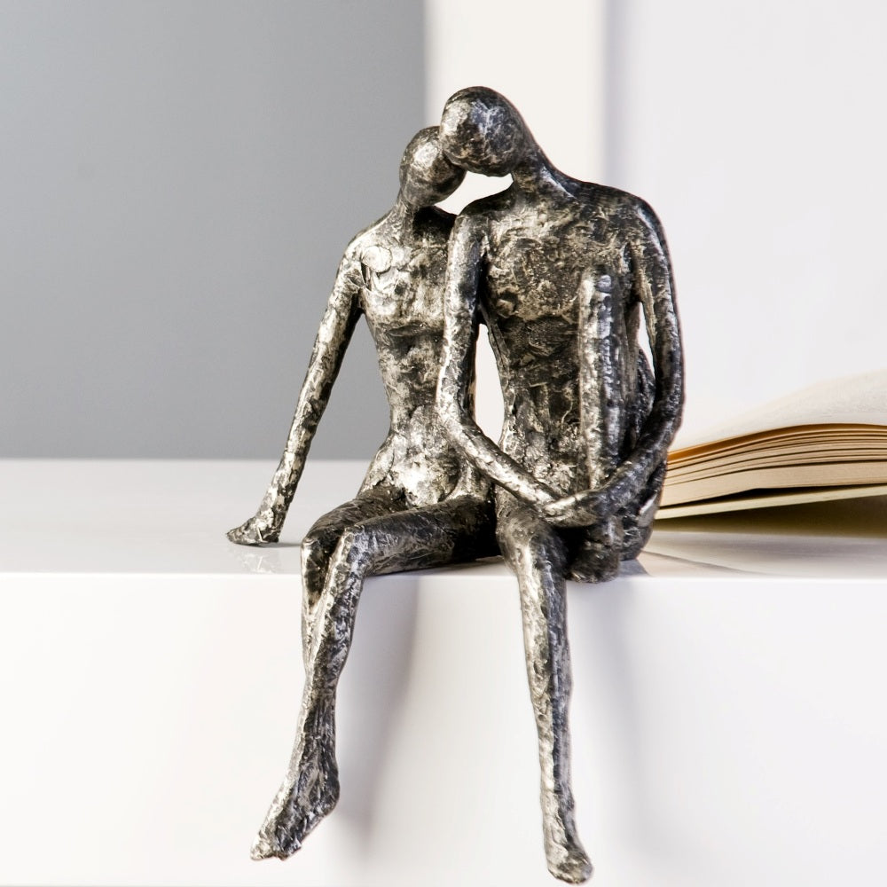 Bei der Skulptur Couple handelt es sich um einen Kantensitzer. Das Pärchen ist aus Kunstharz gefertigt und in Antik-Silber eingefärbt.