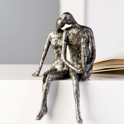 Bei der Skulptur Couple handelt es sich um einen Kantensitzer. Das Pärchen ist aus Kunstharz gefertigt und in Antik-Silber eingefärbt.