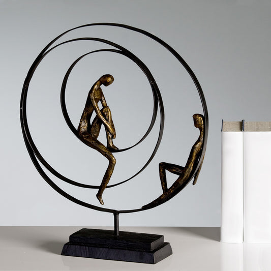 Die Figur Patience besteht aus drei schwarzen Metallringen die auf einer schwarzen Holzbasis stehen. Die in den Ringen sitzenden Figuren bestehen aus hochwertigem Kunstharz in Bronzeoptik 